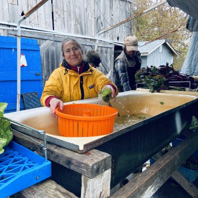 Randi washing root veggies in a large bath tub, wearing fall rain gear, smiling.