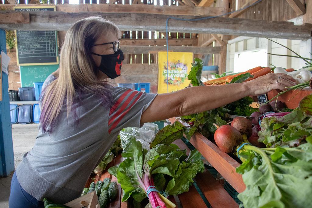 Woman reaching for fresh vegetables on a farm stand in the barn farm store